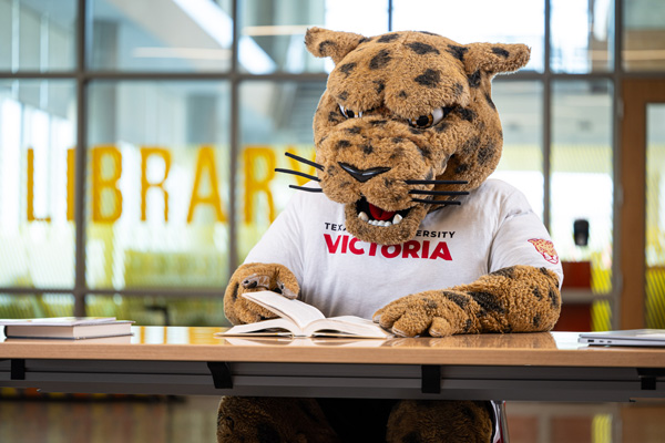 Mascot jaX reading a book in the library
