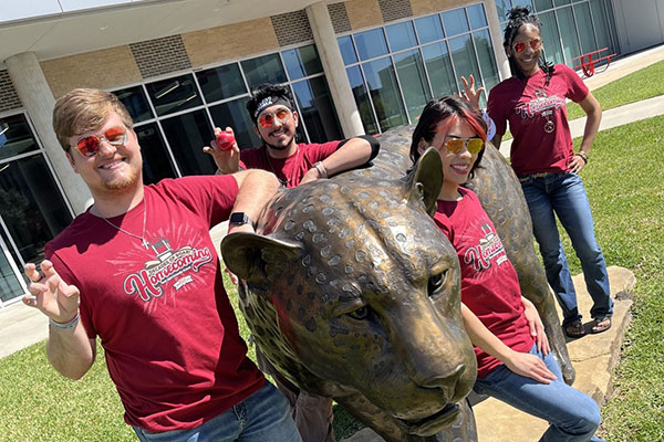 Several student pose in their Homecoming t-shirts by our large jaguar statue near the Commons building.