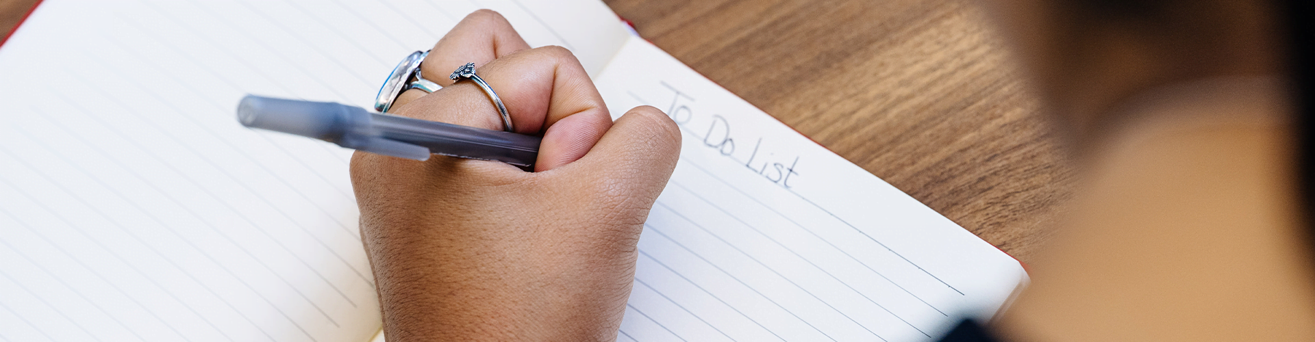 Hand holding a pen, writing in a notebook opened to a to-do list.