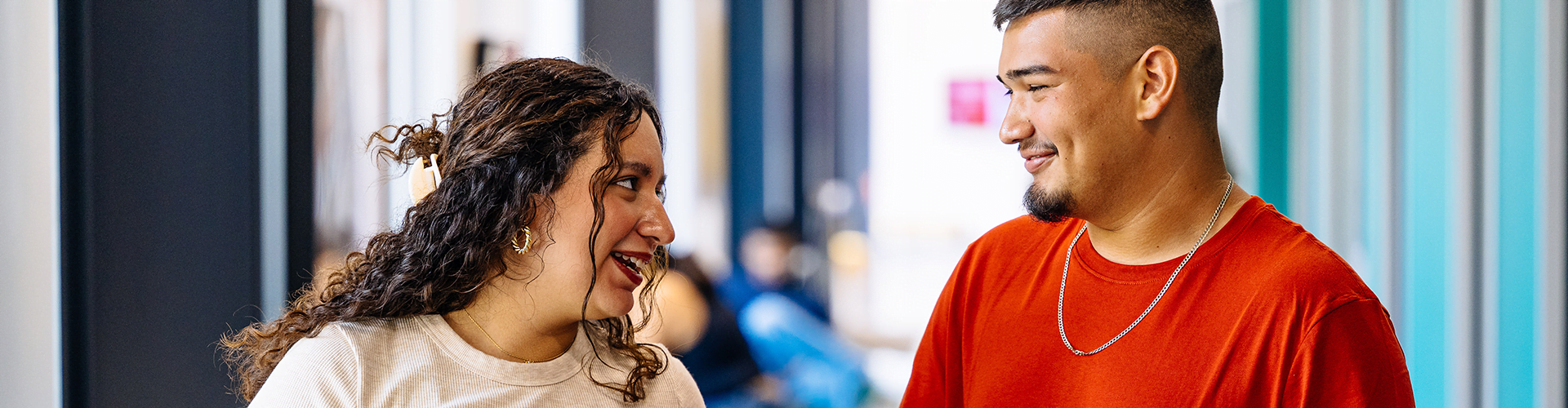 Two people standing indoors, facing each other and talking.