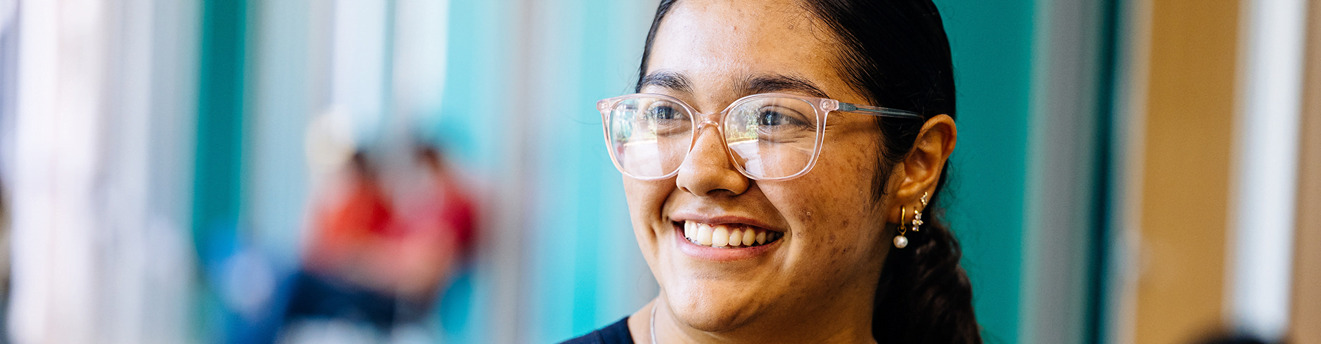 Person with dark hair pulled back, smiling and wearing eyeglasses and small hoop earrings.