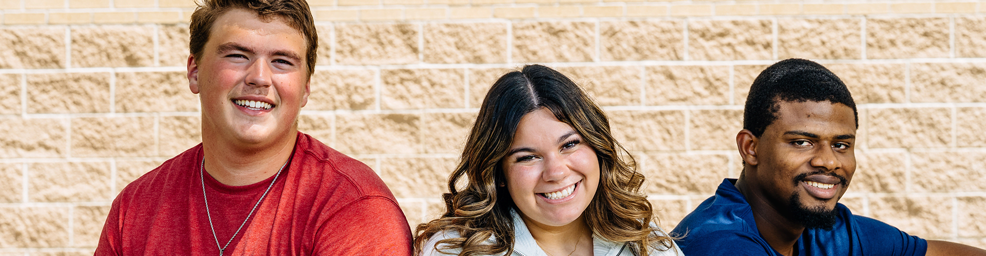 Three people sitting in front of a light-colored brick wall, smiling at the camera.