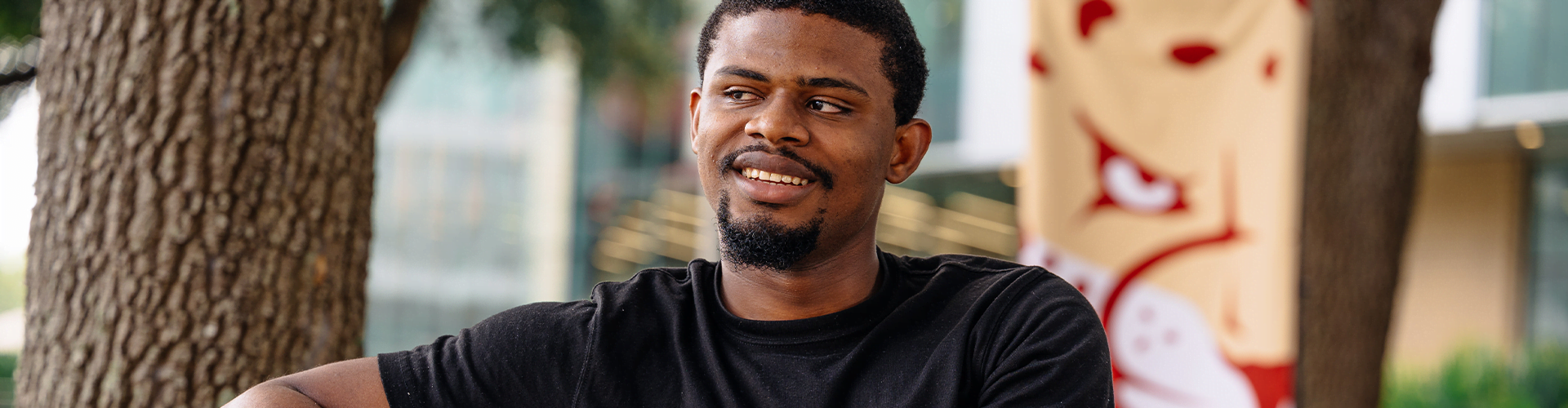 Person sitting outdoors near a tree, wearing a black t-shirt.