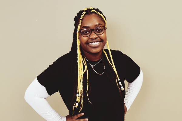 A student with yellow braids, wearing glasses, a black t-shirt over a white long-sleeved shirt.
