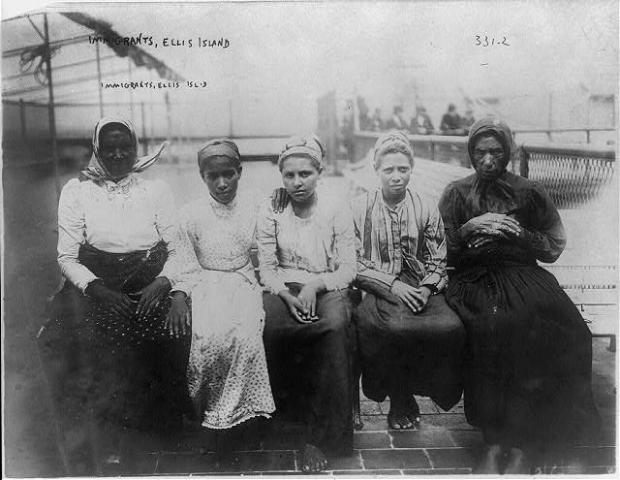 Photograph shows five women immigrants sitting on dock at Ellis Island. Bain, George Grantham, 1865-1944, photographer.