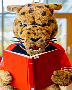 UHV jaguar mascot reading a large red book.