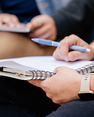 A person seated and engaged in writing activities—holding a notebook and a pen.