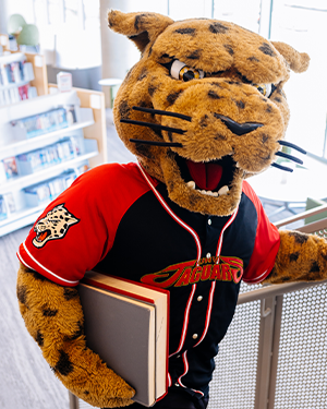 X the jaguar mascot holding book near library shelves