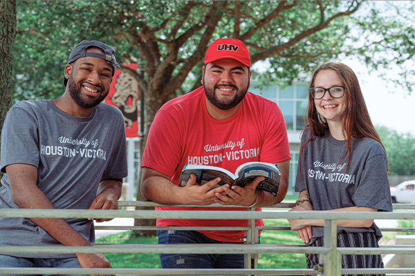 Three students outside, looking at a book.