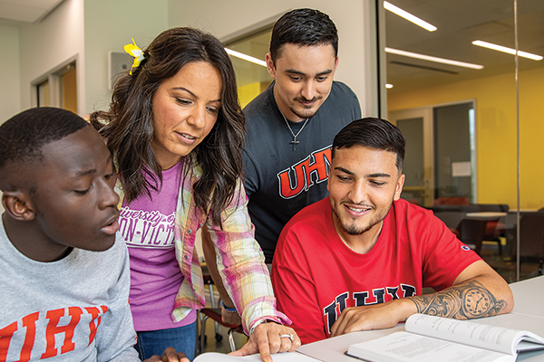 Four students wearing UHV apparel, looking at textbooks.