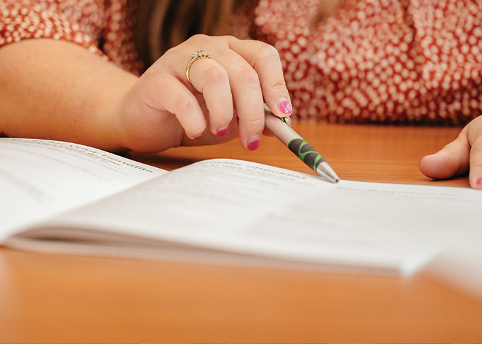 person holding a pen and pointing to information on a book